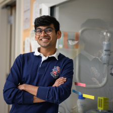 A young man in a rugby shirt stands arms crossed in a lab