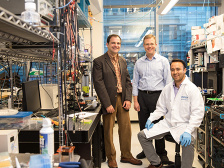 Three men in a lab full of wires and machines.